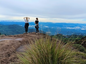 Two individuals standing on a rocky outcrop overlooking a mountainous landscape. - Grace Grand Resort Munnar (Devikolam)