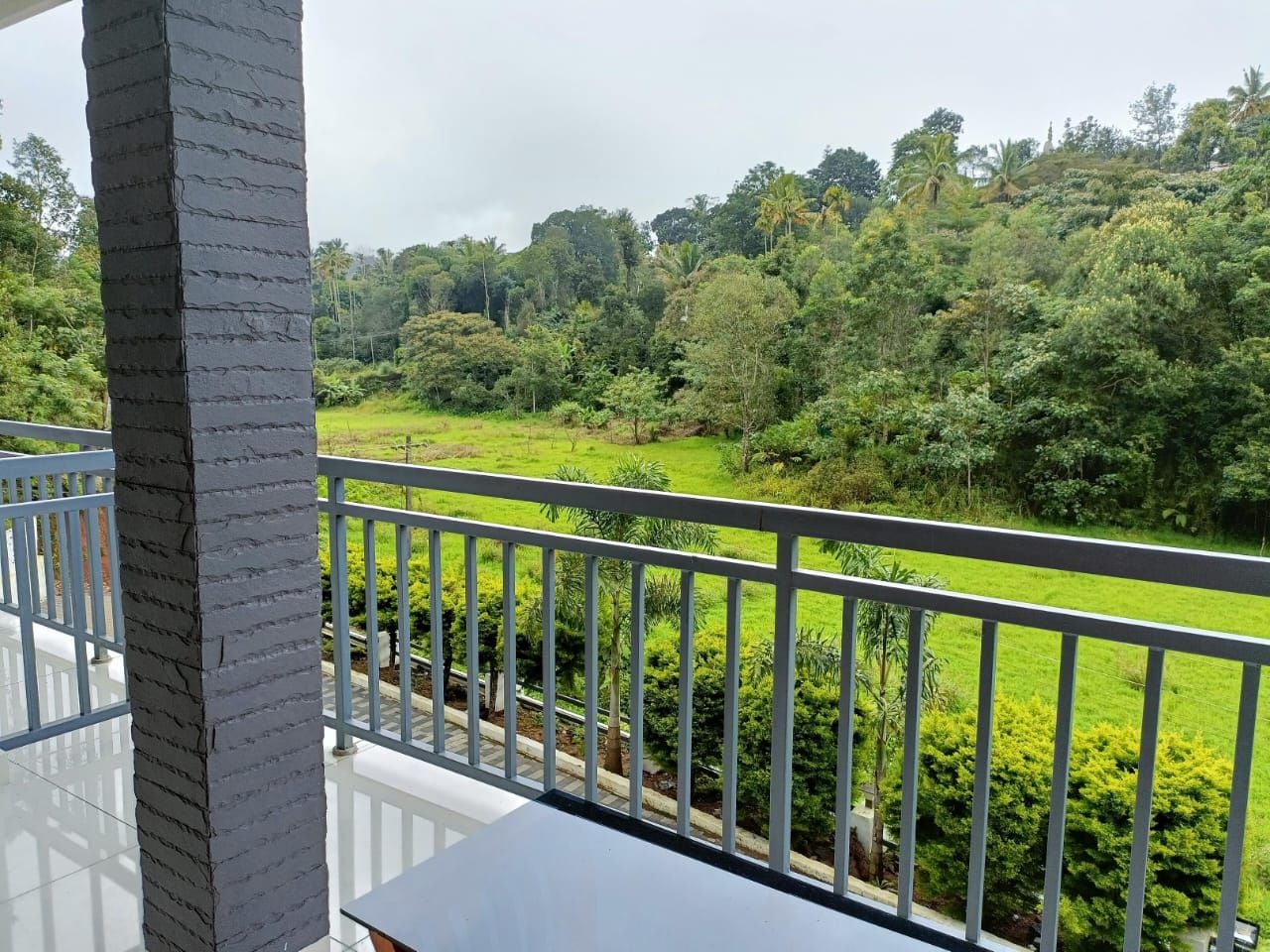 Ein Balkon mit Blick auf eine üppige, grüne Landschaft, darunter eine gepflegte Rasenfläche und dichte Bäume.