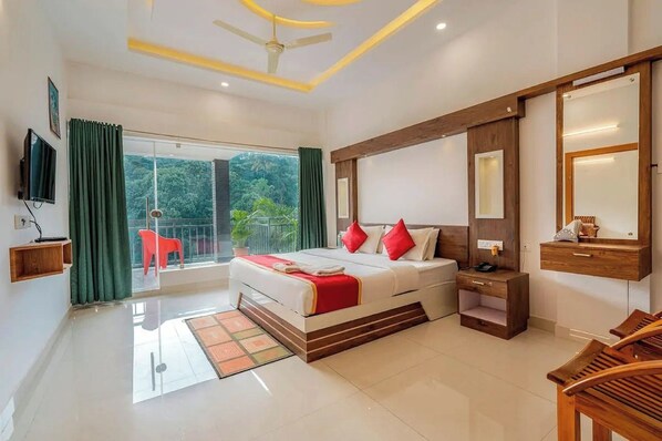 Habitación de hotel con cama, mesita de noche, espejo, televisor y balcón con vistas a zonas verdes.