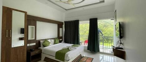 A hotel room with a bed, a TV, a ceiling fan, a balcony, and a view of greenery.
