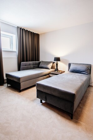 A hotel room with two single beds, a bedside table with a lamp, and a window with curtains.
