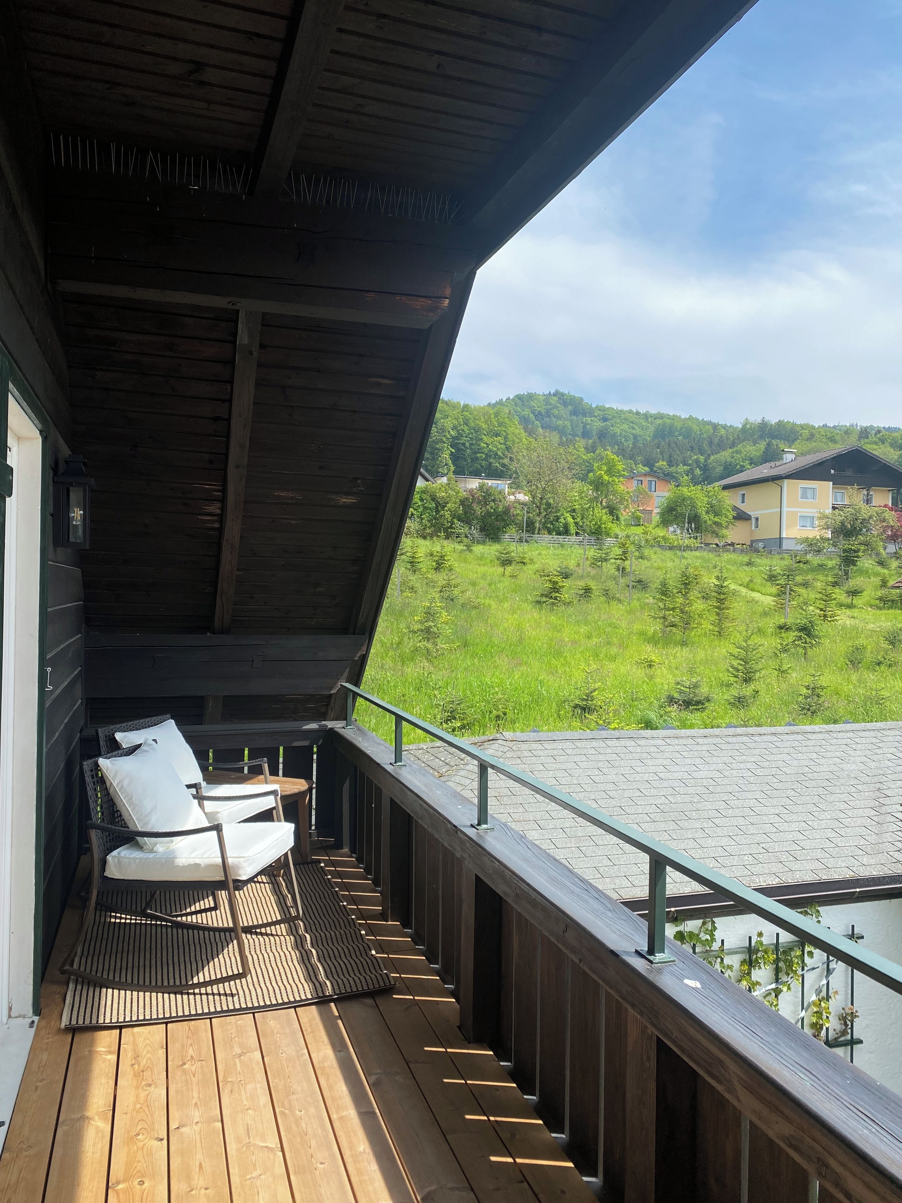 Une terrasse en bois avec des meubles d’extérieur, une vue sur un paysage verdoyant et un bâtiment en arrière-plan.