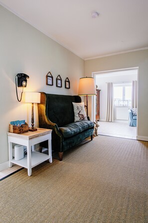 A living room with a sofa, a side table, a lamp, a telephone, and a framed picture on the wall.