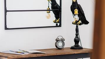 Une table à manger avec un cadre en métal noir, deux poufs noirs à texture tissée, une horloge murale noire et une figurine d’oiseau noir tenant une ampoule.