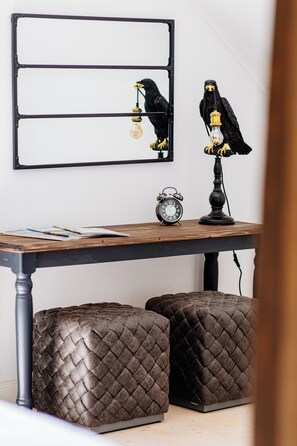 A dining table with a black metal frame, two black ottomans with a woven texture, a black wall clock, and a black bird figurine holding a light bulb.