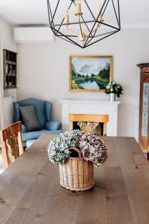 A dining table with a wicker basket containing flowers, a blue sofa, a fireplace, and a chandelier.