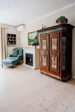 A living room with a blue armchair, a fireplace, and a wooden cabinet with floral designs.