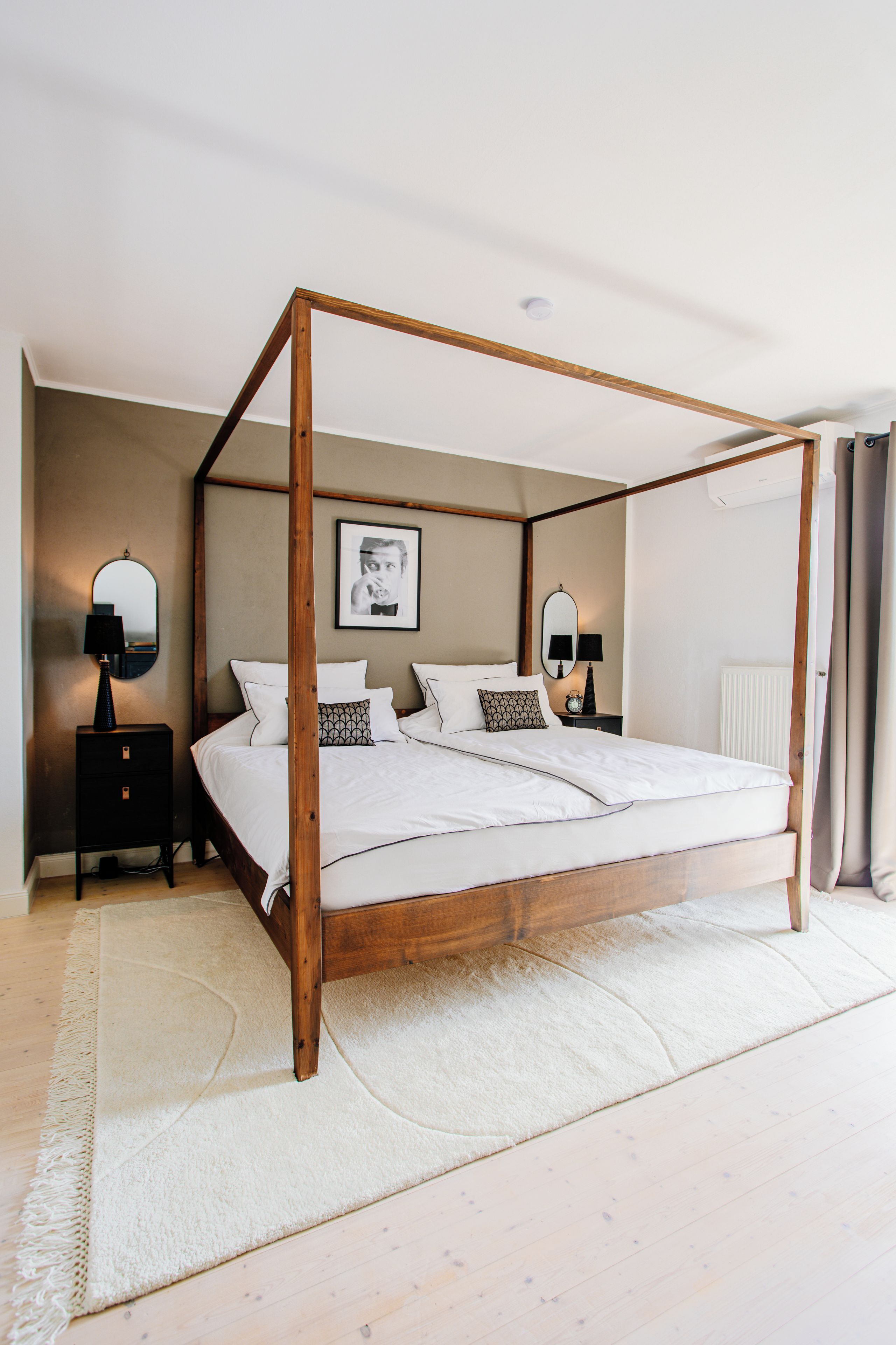 Un lit à baldaquin avec une structure en bois, une literie blanche et un tapis blanc posé sur un plancher en bois.