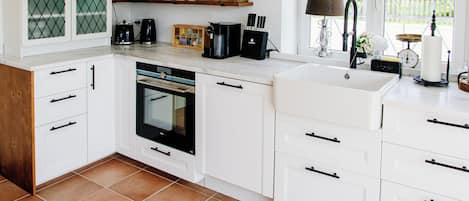 Une cuisine moderne avec des meubles blancs, un four encastré et une grande fenêtre donnant sur un paysage verdoyant.