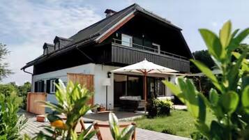Ein modernes, zweistöckiges Haus mit Balkon, Sitzgelegenheit im Freien und einem Garten.