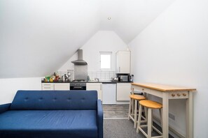 A compact kitchenette with a sofa, a small table with stools, and a window. - Spacious Top-Floor Flat near Finsbury Park (Greater London)