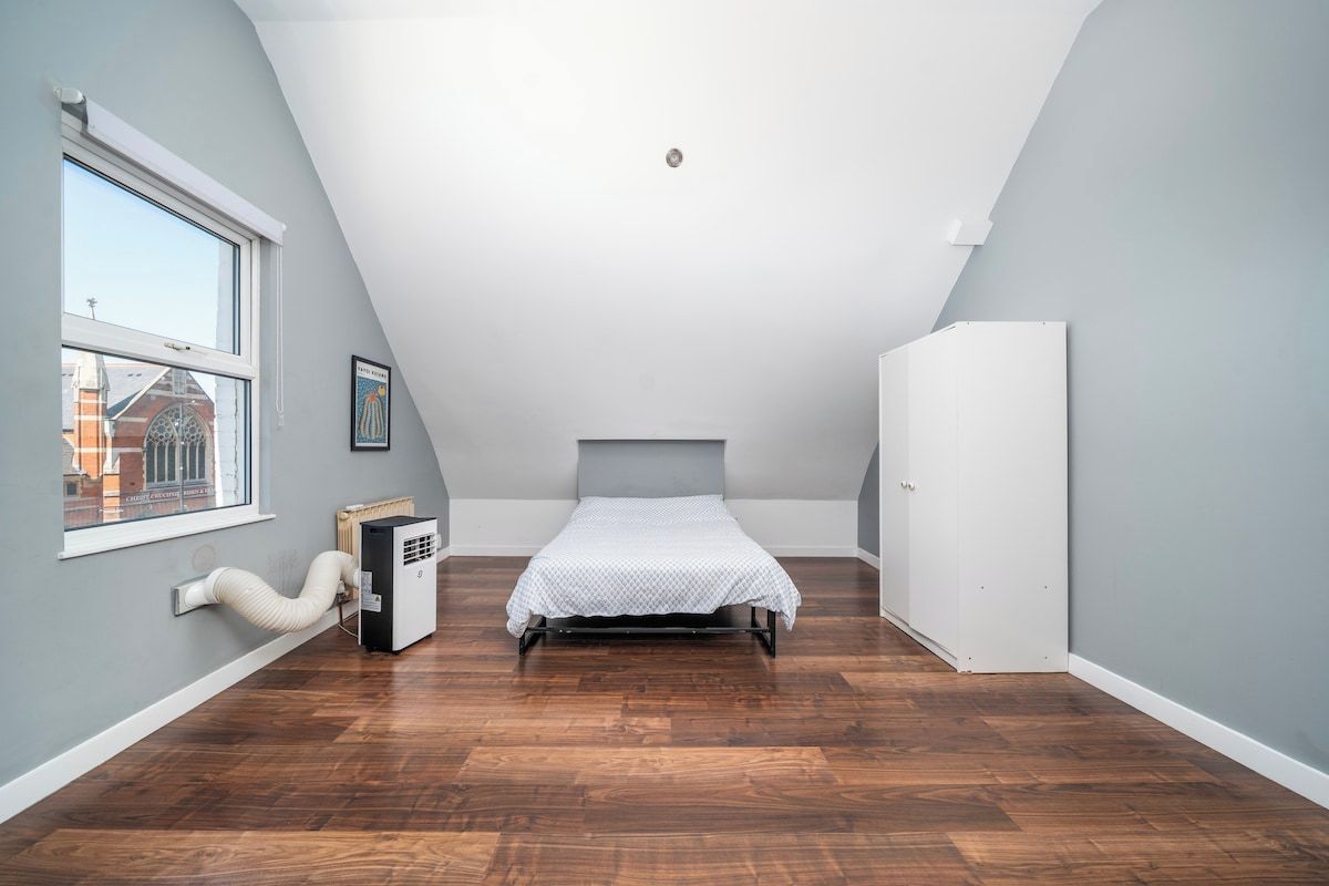 Une chambre avec un plafond en pente, un lit, un radiateur et une fenêtre.