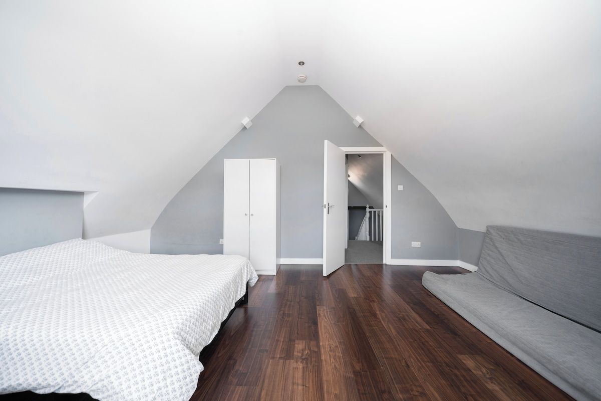 Un dormitorio con techo inclinado, una cama, un sofá gris y un armario.