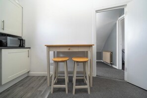 A small kitchenette with a microwave, a table with two stools, and a door leading to a stairwell. - Spacious Top-Floor Flat near Finsbury Park (Greater London)