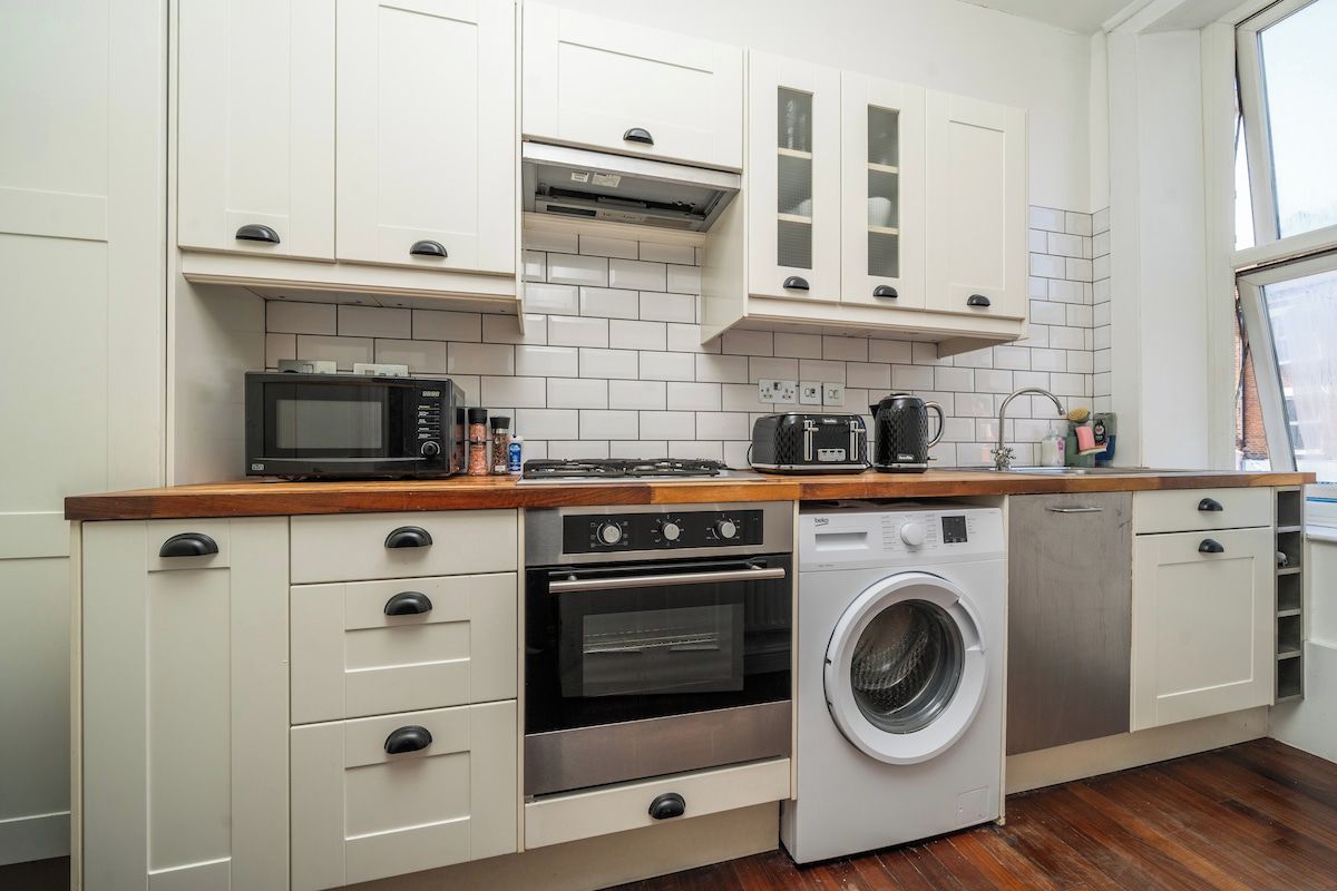 Une cuisine compacte avec des meubles blancs, un four à micro-ondes, un four traditionnel et un lave-linge.