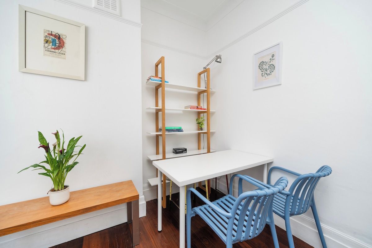 Une pièce avec un bureau blanc, des chaises bleues, une bibliothèque en bois et une plante en pot.