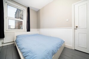 A bedroom with a single bed, a window with curtains, a white door, and a radiator. - Stylish Victorian Flat near Finsbury Park (Greater London)