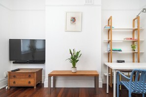 A room with a flat-screen TV, a wooden bench, a small table, a blue chair, and a bookshelf. - Stylish Victorian Flat near Finsbury Park (Greater London)