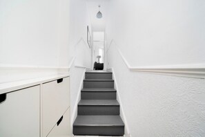 A narrow staircase with white walls and a dark floor leading to a room with a bed and a nightstand. - Stylish Victorian Flat near Finsbury Park (Greater London)