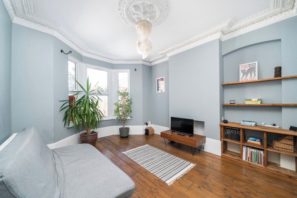 Una sala de estar con sofá, televisor, suelo de madera, candelabro y estantería.