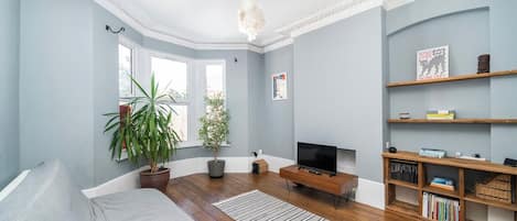 A living room with a sofa, a television, wooden flooring, a chandelier, and a bookshelf.