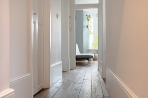 Un pasillo con paredes blancas y piso de madera que conduce a una habitación con cama y una planta colgante.