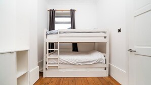 A bunk bed room with white walls, a wooden floor, and a window with curtains. - Bright Garden Flat with Private Outdoor Space (Greater London)