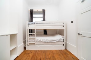 Habitación con literas, paredes blancas, suelo de madera y ventana con cortinas.