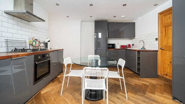 A modern kitchen with a round glass table, white chairs, a built-in oven, and grey cabinets. - Bright Garden Flat with Private Outdoor Space (Greater London)