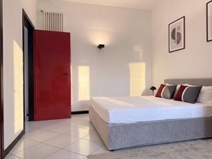 Ein modernes Schlafzimmer mit einem Bett, einer roten Tür, einem Heizkörper und einem gerahmten Bild an der Wand.