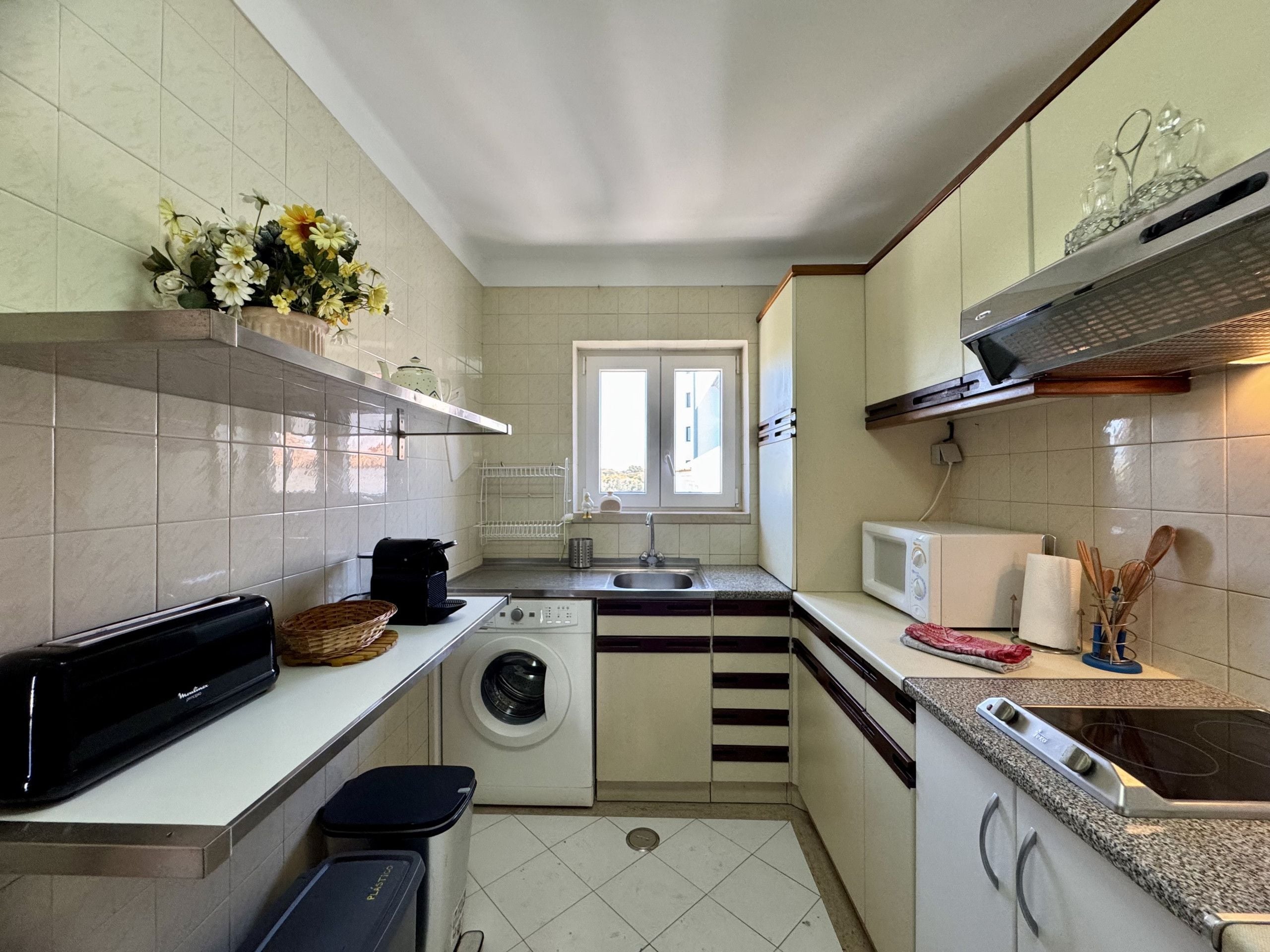 Cocina compacta con lavadora, microondas y un ventanal pequeño.