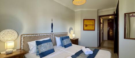A hotel room with a large bed, a bedside table with a lamp, a wall-mounted artwork, and a door leading to another room.