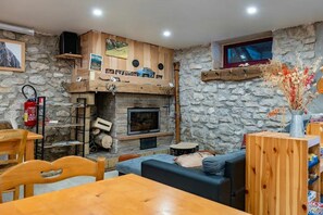 Ein gemütliches Wohnzimmer mit Steinwand, Kamin, Fernseher und Holztisch.