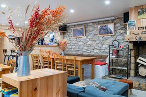 A rustic interior with a stone wall, wooden furniture, a metal vase with dried plants, and a fireplace. - Chambre en demi pension"Les Carlines (Vassieux en Vercors)