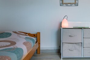 A bedroom with a wooden bed, a bedside table with a lamp, and storage drawers. - Chambre en demi pension"Les Carlines (Vassieux en Vercors)