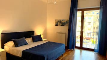 A bedroom with a bed, a nightstand, a wall-mounted painting, and a view through a window with curtains.
