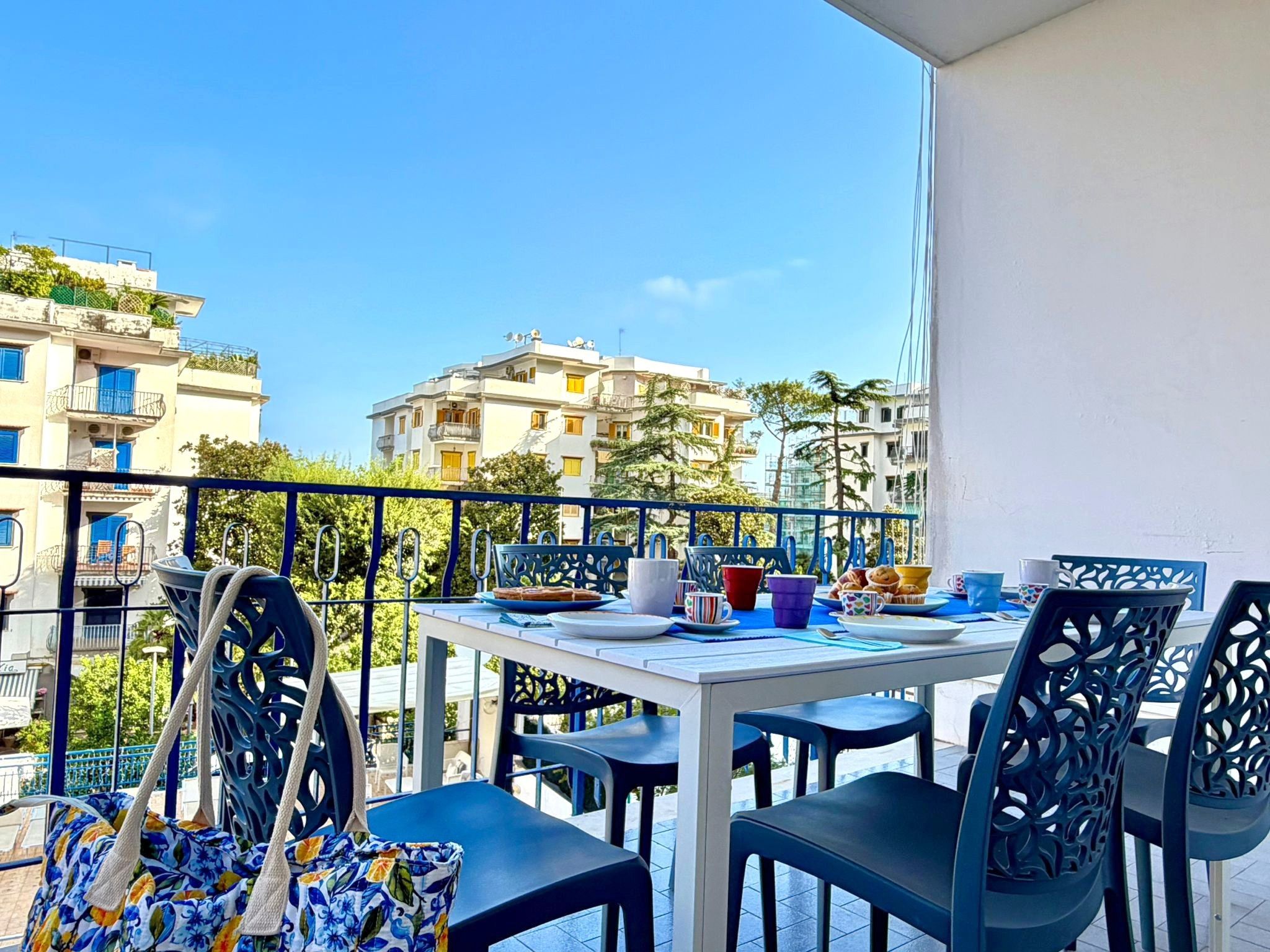 Un balcon avec une table préparée pour le petit-déjeuner, donnant sur un quartier résidentiel avec ses immeubles.