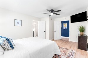 A bedroom with a bed, a ceiling fan, a TV on the wall, and a door leading to another room. - Pet-friendly Pensacola Escape - Sleeps 10 (Pensacola)