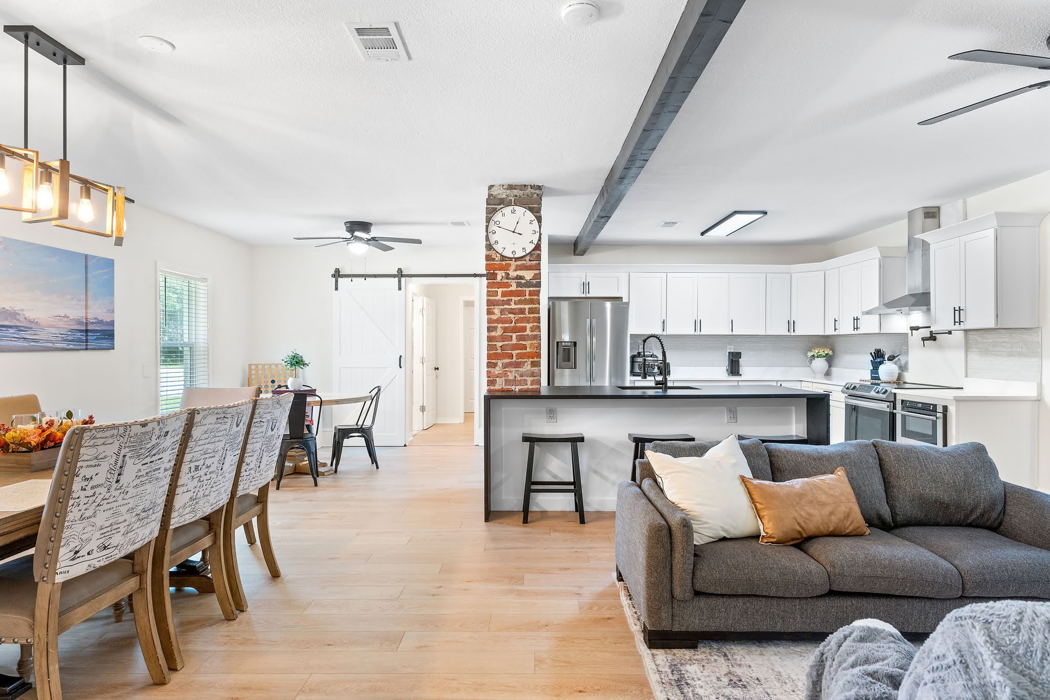 A modern kitchen with white cabinets, a central island, and a brick accent wall.