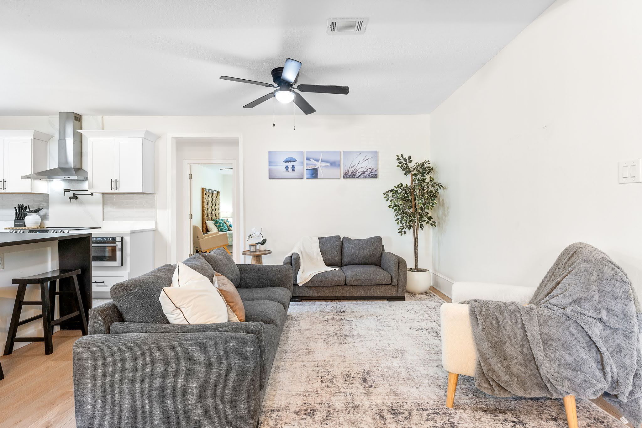 A modern living room with a grey sofa set, a coffee table, and a dining area with a kitchen in the background.