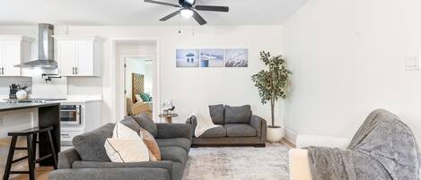 A modern living room with a grey sofa set, a coffee table, and a dining area with a kitchen in the background.