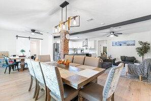 A modern kitchen with white cabinets, a brick accent wall, and a dining area with a wooden table and patterned chairs. - Pet-friendly Pensacola Escape - Sleeps 10 (Pensacola)