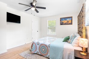 A bedroom with a bed, a ceiling fan, a window with blinds, a painting on the wall, and a woven wall decoration. - Pet-friendly Pensacola Escape - Sleeps 10 (Pensacola)