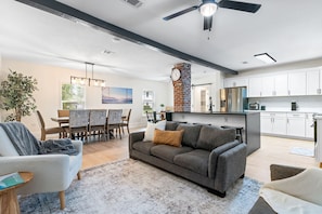 A modern living room with a grey sofa, a dining area with a wooden table, and a kitchen with white cabinets and stainless steel appliances. - Pet-friendly Pensacola Escape - Sleeps 10 (Pensacola)