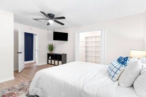 Une chambre à coucher comprenant un lit, un ventilateur de plafond, une télévision, une armoire et une fenêtre avec des stores.