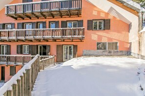 Un edificio de varios pisos con balcones, barandas de madera y suelo cubierto de nieve.