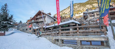Un pueblo en la montaña cubierto de nieve, con edificios de madera y banderas que señalan servicios como taquillas para esquíes y cafetería.