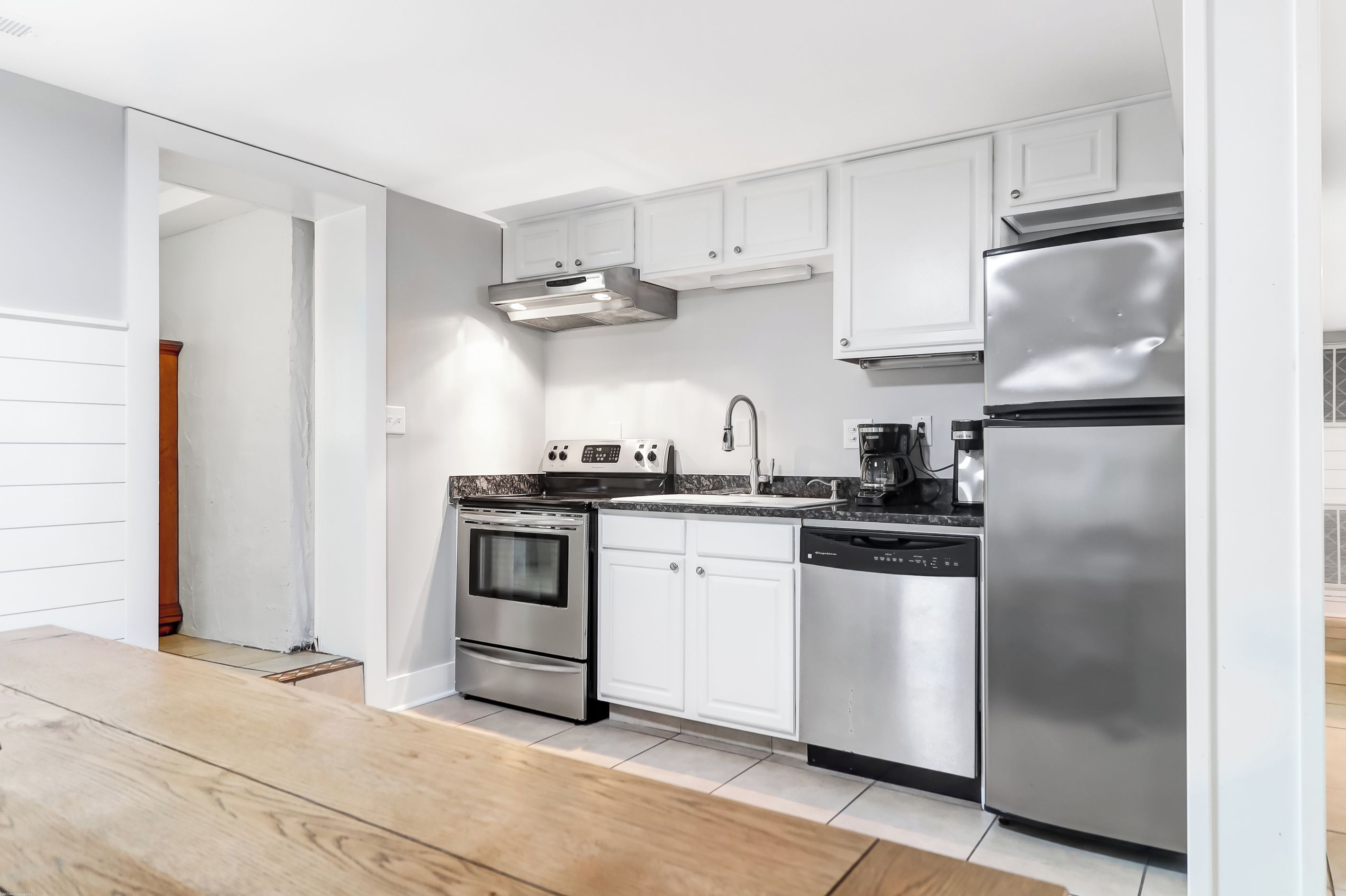 A modern kitchen with stainless steel appliances, white cabinetry, and a wooden floor.