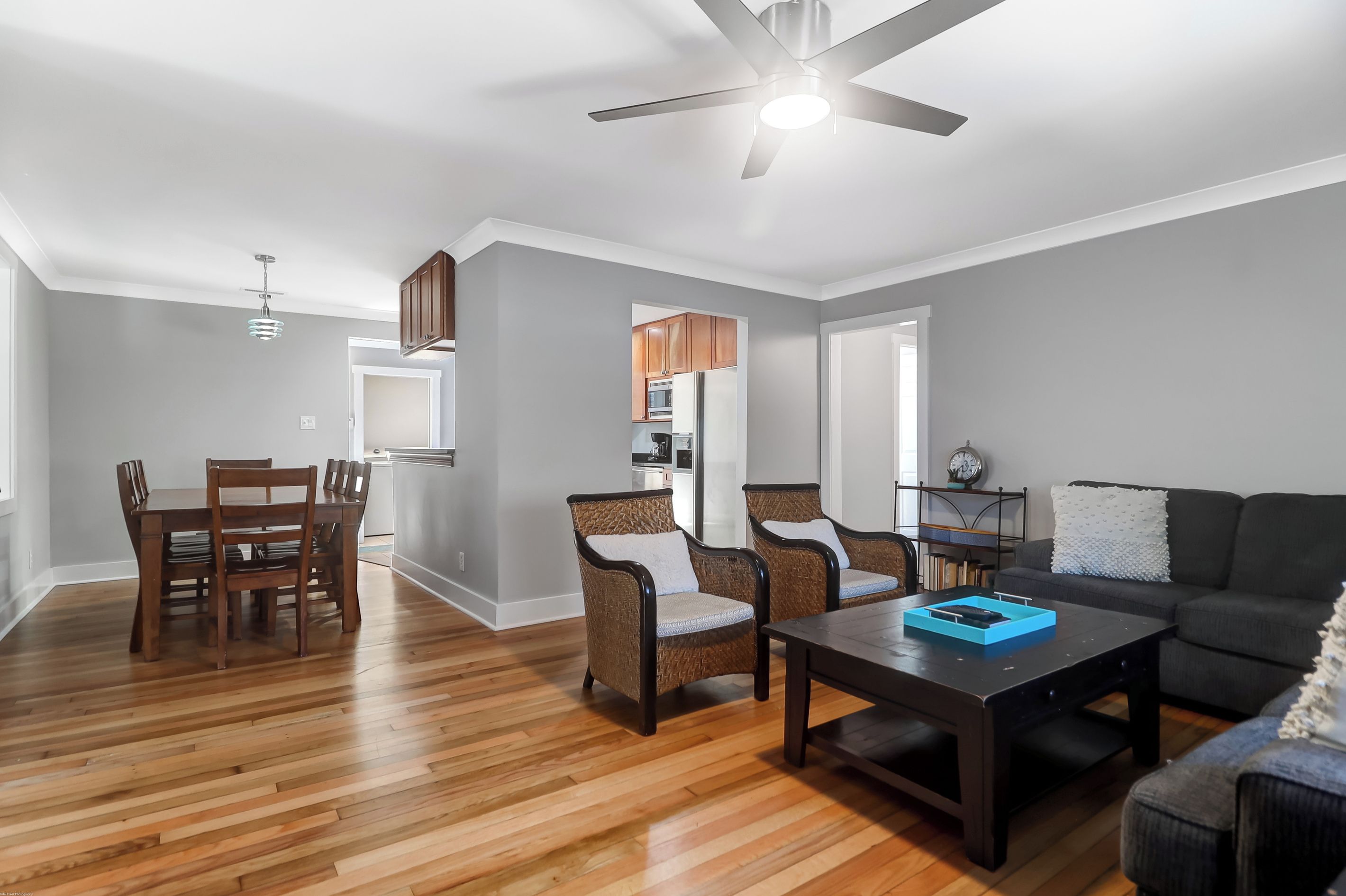 A modern living room with a dark brown sofa, two wicker chairs, a wooden coffee table, and a ceiling fan.