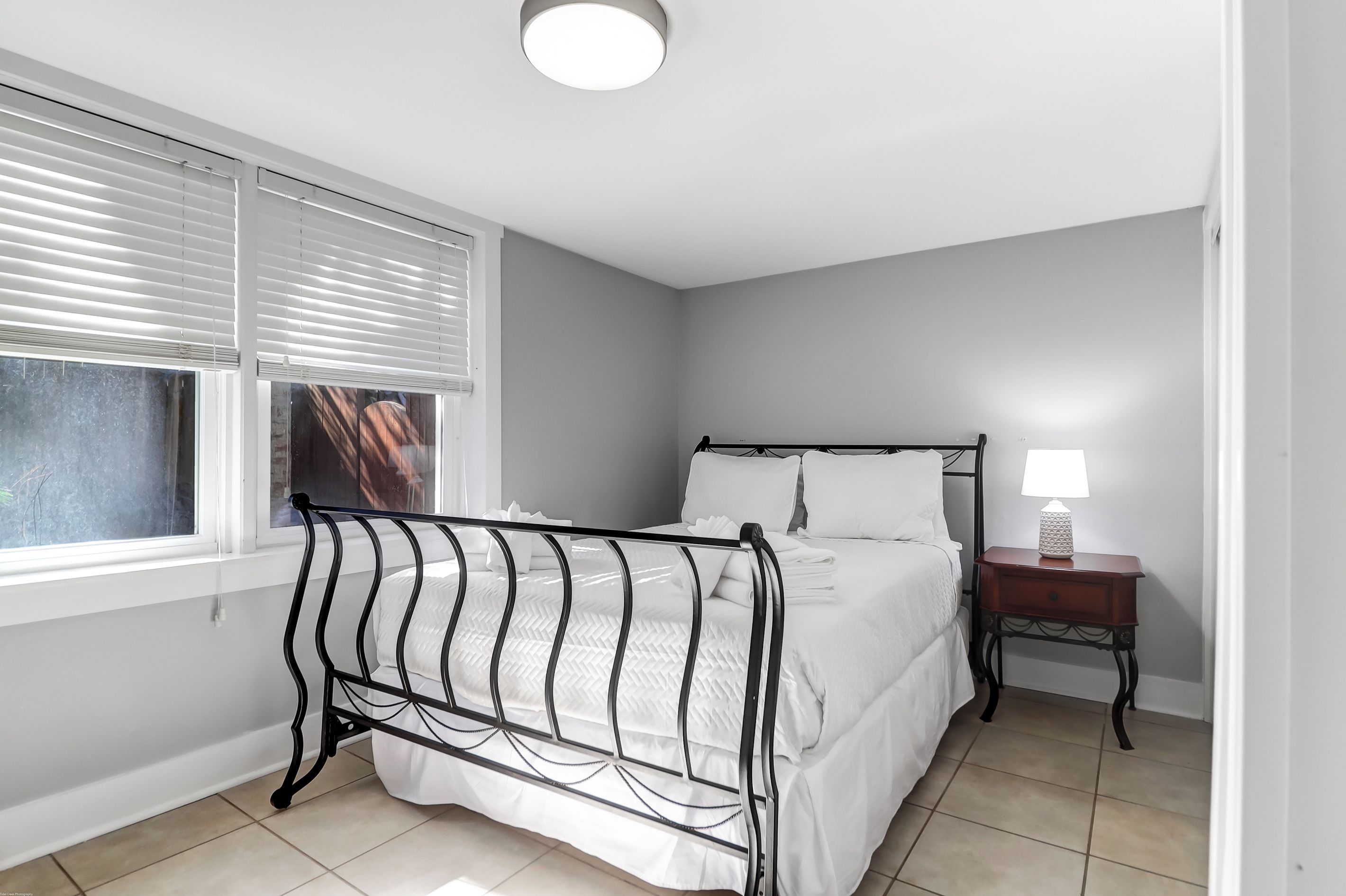 A bedroom with a bed, a bedside table with a lamp, and a window with blinds.